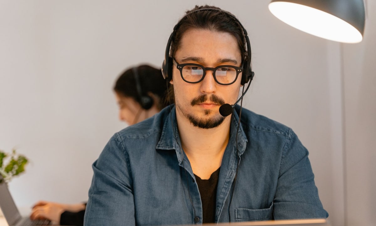 Customer service agent with a headset at a desk next to a live chat screen